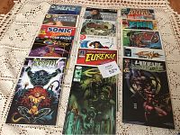 Top view of 15 comic books in protective covers laid out on a lace cloth, showing a variety of titles including Silk, Saiko Lavender, Sonic the Hedgehog, Gold Digger and others.