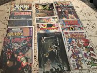 14 comic books in plastic protective covers arranged on tablecloth to show front covers of each.
