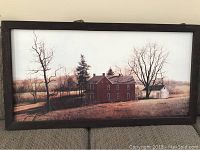 Framed landscape picture showing a brown house among trees in an autumnal or winter scene, with a dark wooden frame.