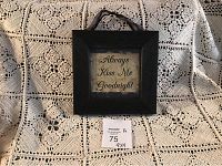 Front view of the square black framed sign with the phrase 'Always Kiss Me Goodnight' on a cream background hung by a black strap.