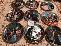 Nine decorative plates arranged on lace fabric, showing various scenes from The Wizard of Oz movie, with gold rims.