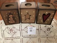Photo of three small tissue box covers placed side by side on a lace doily, showing holiday designs including a snowman, star cutout, and heart cutout.