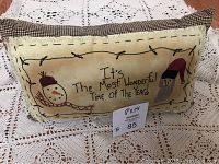 Photo of rectangular Christmas pillow featuring embroidered text 'It's The Most Wonderful Time Of The Year' with snowman and Santa characters, set on lace surface.
