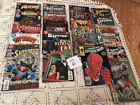 Lot of comic books featuring Batman, Spiderman, Superman, Superboy, Robin, Catwoman, and Phantom laid out on a cloth surface.