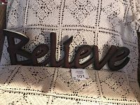 Full view of the 'Believe' standing sign placed on a lace textured fabric surface showing length and style