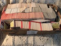 Box filled with a large quantity of sports cards laid flat, showing the edges and backs with various colors, mostly beige, white, and red backs.