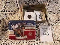 Metal tin container for Marbles Shooting Games with lid off, showing some coins inside in protective flips