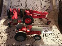 Top-down photo showing three red metal tractor models on a lace tablecloth, displaying varying designs and red and grey paint.