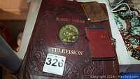 Three leather items on a table: a large engraved Radio Times Television leather cover, a smaller 7.5x4.75 notebook with visible writing and a calendar, and a smaller red hand-tooled notebook cover with pencil.
