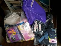 Six bags of fabric remnants including vintage beaded corset pieces in plastic bags on a table with other fabric remnants and craft kits visible.