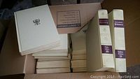 Top view of Encyclopaedia Britannica 25-volume set in beige hardcover with some books out of order visible in a cardboard box.