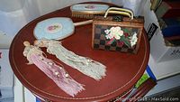 Samsonite round leather luggage top view with vanity brush, mirror, and floral patterned accessory box with tassels and vintage headwear