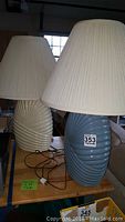 Pair of ceramic lamps on table, ivory on left, blue on right, both with cream pleated shades