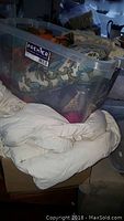 Photo of plastic bin filled with assorted printed fabrics and light colored comforter beside it