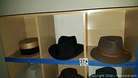Three men's vintage hats displayed in wooden cubbies, including a straw boater, a black felt hat, and a brown wool hat with embellishment.