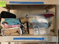 Large bin filled with assorted linens and folded fabrics including crocheted pieces and what appears to be quilted or embroidered textiles.