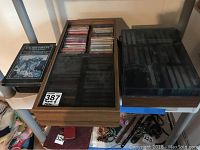 Photo of two cassette storage cabinets and several cassette tapes on a shelf, with some tapes visible inside the wooden cabinet.