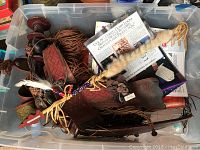 Top view of plastic bin showing leather items including tassels, braided pieces, paper documents, and arrow with fur and bead embellishments.