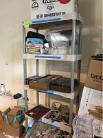 Front view of the plastic utility shelf with items stored on all shelves including fabric, boxes, and household goods