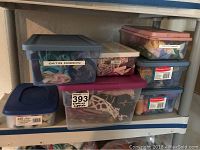 Seven plastic containers with labels showing contents such as satin ribbon and crafting supplies, stacked on a shelf.