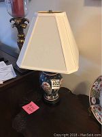 Full view of the porcelain table lamp showing blue base with red and white floral patterns and white lampshade.