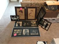 Eight framed portraits, silhouette art, and photographic collages arranged on the floor and leaning against boxes.