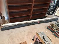 Three rolls of backdrop fabric (black, white, gray) placed on carpet floor under bookshelf with some miscellaneous items nearby.