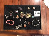 Overview of all 21 pieces of assorted rings, earrings, and bracelets displayed on black fabric