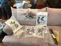 Five Japanese art decorative tapestries displayed on a beige couch with colorful embroidery featuring flowers and birds, some with Japanese characters.