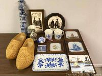 Overview of collection including carved wooden shoes, framed tiles, mugs, vase, tray, small ceramic item, and string of painted wooden shoes.