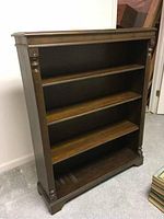 Front view of the dark stained solid wood bookcase showing three shelving levels and carved column accents on the front sides.