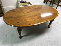 Full view of the top and legs of the oval coffee table on carpet, showing wood grain and finish.