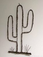 Barbed wire cactus shaped wall art hanging on wall, showing full cactus silhouette with two arms and ground plant shapes.