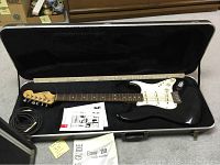 Full view of black Fender Stratocaster in open hard shell case with cable and Envoy 110 manual
