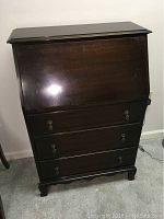 Front view of a vintage dark wood drop front butler's desk with three drawers and brass handles, closed position.