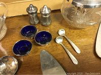 Photo showing sterling silver salt cellars with cobalt blue glass liners, silver salt spoons, and individual salt shakers.