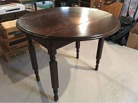 Side view of antique round wooden table with drop leaf sides and turned legs.