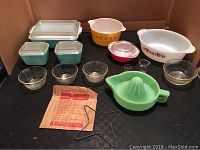 Full lot overview showing variety of Pyrex bowls, turquoise refrigerator dishes, glass bowls, Jadite juice reamer, metal mold, and small measured cups.