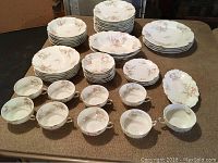 52 piece Limoges Depose France china set arranged on a surface showing cups, plates, and bowls with floral pattern and gold trim.