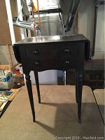 Front view of mahogany sewing stand with two drawers and leaves down, showing turned legs and wooden knobs on drawers.