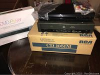 Photo showing Memorex DVD player in plastic sealed, placed atop RCA CD player and original RCA CD player box below them
