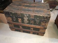 Front angled view of the antique travel trunk showing oak slats, metal reinforcements, and central lock hardware.