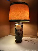 Lamp turned on showing warm glow from textured golden brown shade on porcelain floral base.