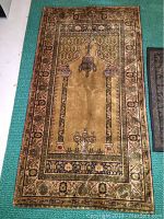 Full view of the woven prayer rug showing detailed border and central arch pattern with hanging lamps and floral motifs