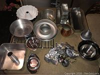 Wide shot showing a large assortment of metal baking pans including bundt pans, round cake pans, tube pans, and small baking molds. Includes some mixing bowls, vintage cookie cutters, and a funnel.