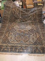 Full view of the carpet partially draped over a surface with visible floral and geometric patterns in blue, beige and gold tones.