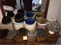 Vintage hats displayed on dresser with several vintage hat boxes and a gray wig in the background.