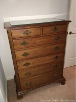 Front view of 7 drawer wooden chest with brass handles and glass top plate.
