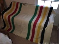 Full view of the Hudson Bay wool blanket draped over furniture showing the four colored stripes: black, green, red, and yellow on cream background.