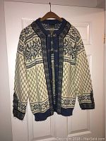 Full view of Dale of Norway ladies' wool sweater in blue and white knit pattern, showing front metal clasps and overall design.